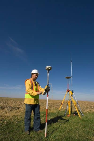 Licensed land surveyor using GPS and tripod instruments to measure property boundaries after storm erosion