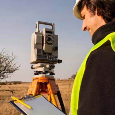 Licensed land surveyor measuring ground elevation to confirm whether an existing elevation certificate is still accurate