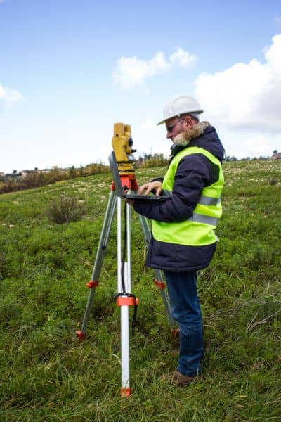 A land surveyor using a total station to capture accurate elevation data for a topographic survey during renovation planning