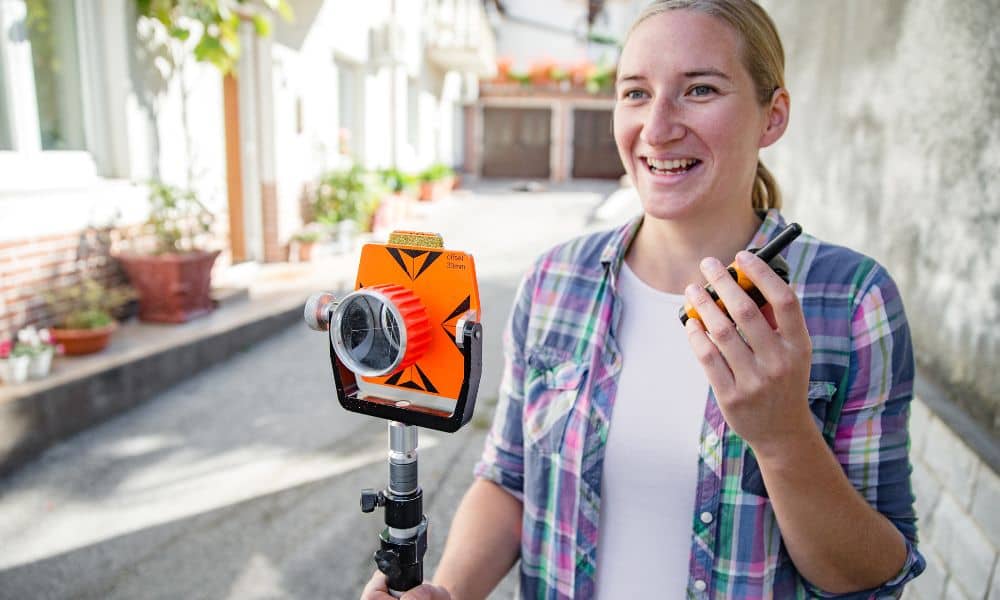 A professional surveyor using equipment to measure property boundaries in a residential neighborhood while evaluating land survey cost