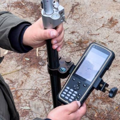 A licensed land surveyor uses surveying equipment to measure elevation on-site, ensuring accurate data for flood risk assessments and property planning.